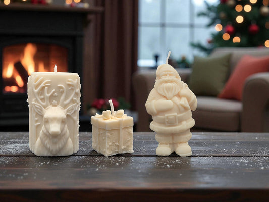 Three white candles shaped like a dragon, castle, and Santa Claus on a wooden table with a fireplace and Christmas tree in the background.