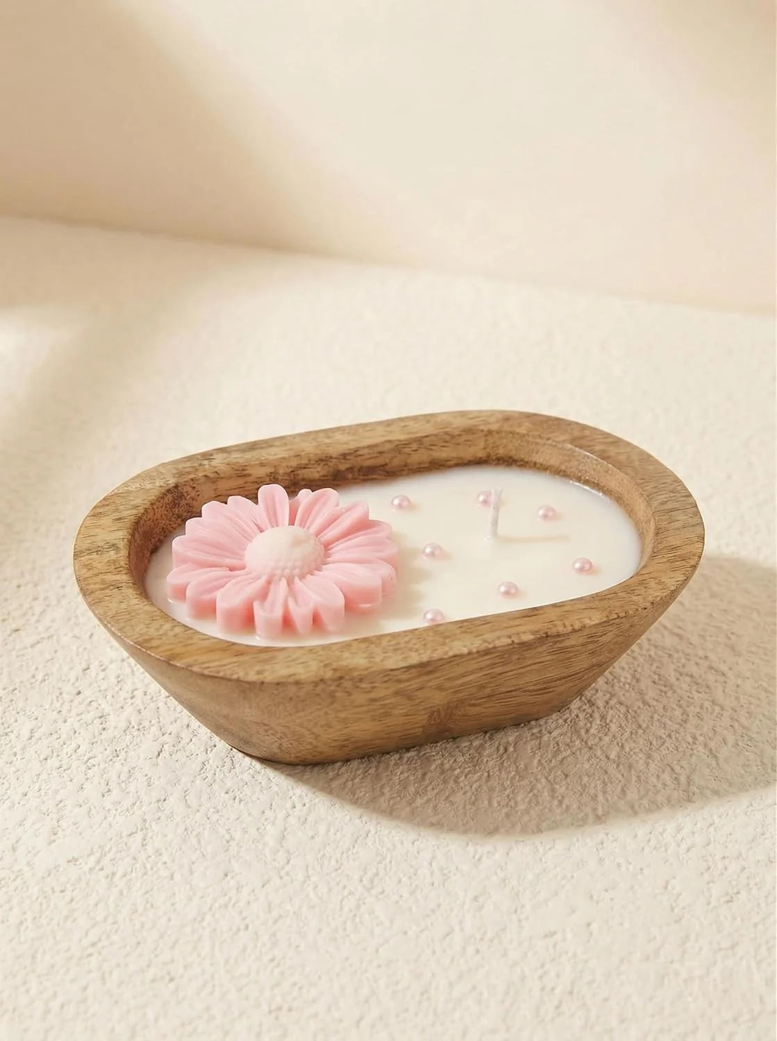 Wooden bowl with a candle and a pink flower-shaped soap on a beige background