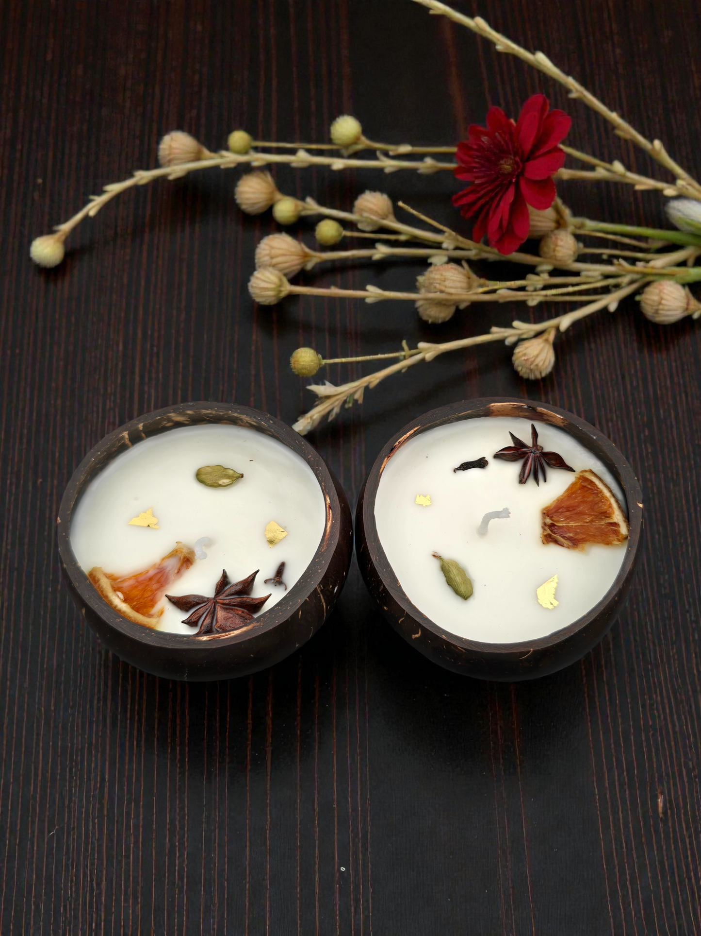 Two candles with botanical elements on a dark surface with flowers.