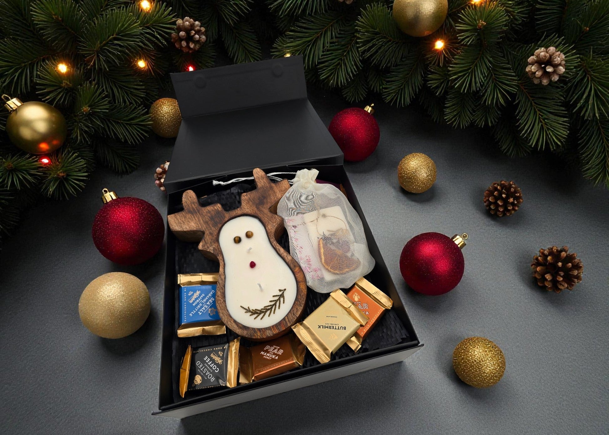 Box of assorted chocolates with a snowman design on a festive background with Christmas ornaments.