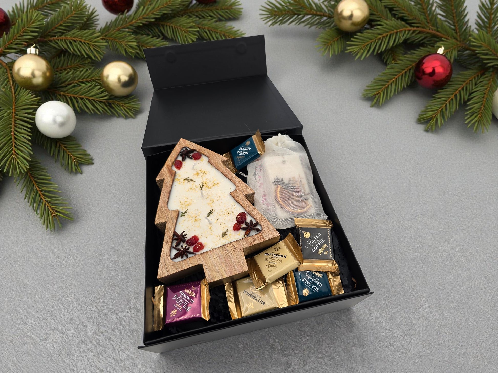 Gift box with assorted items on a gray surface with Christmas decorations.