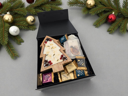 Gift box with assorted items on a gray surface with Christmas decorations.