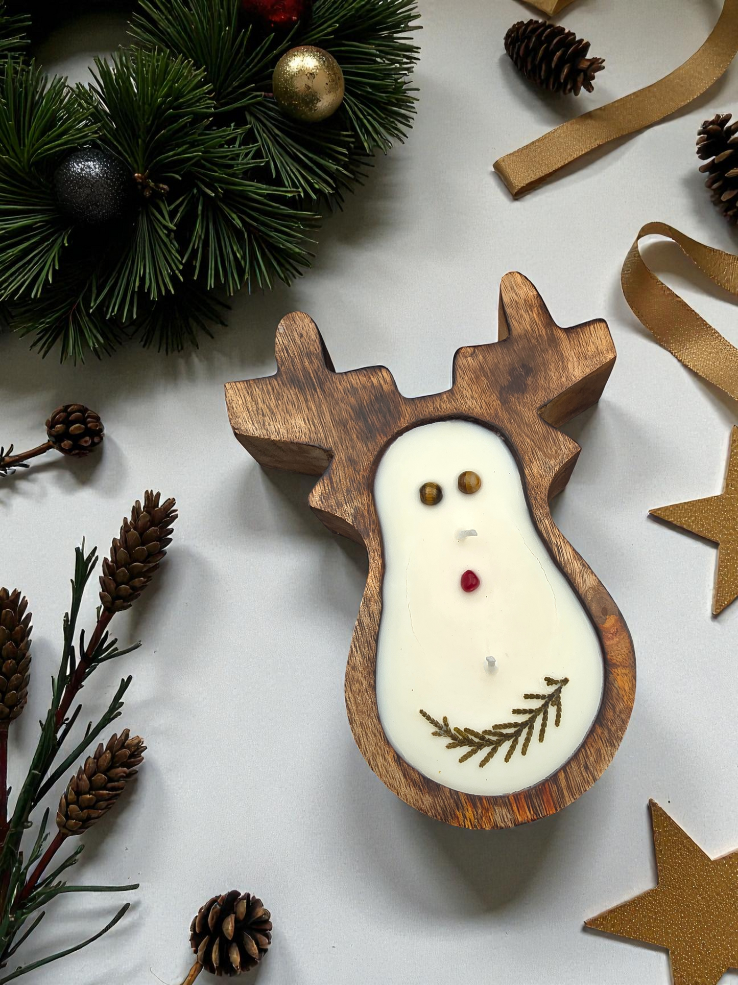 Wooden reindeer-shaped candle with Christmas decorations on a white surface