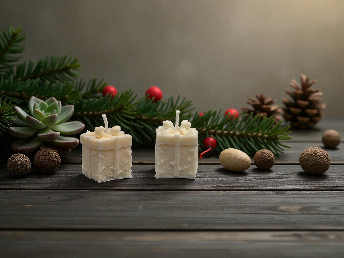 Two white square candles on a wooden surface with Christmas decorations including pine branches, berries, and pinecones.
