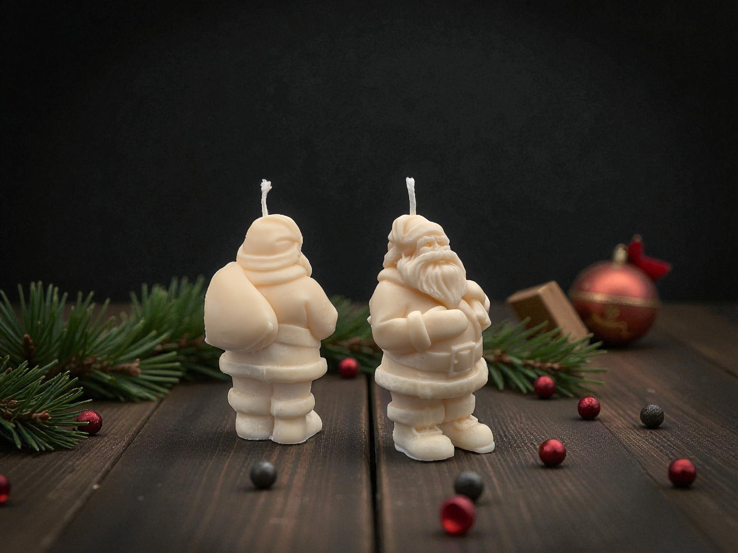 Two Santa Claus-shaped candles on a wooden surface with Christmas decorations.